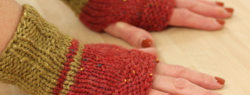 hands modelling hand-knitted fingerless mittens in 2 colours