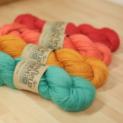 4 skeins of differently coloured mohair-wool blend yarn, (green, orange, coral and red), lying flat on a counter